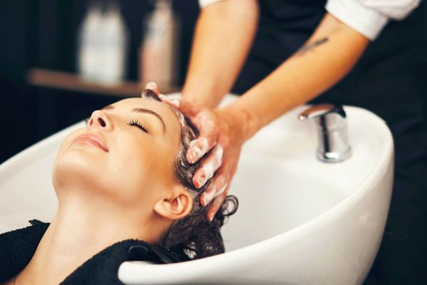 Soap, massage and hairdresser with client in spa, relax and basin for wash and treatment. Hands, salon and hairstyle or balayage dye for happy customer person, keratin or scalp shampoo for hair care.