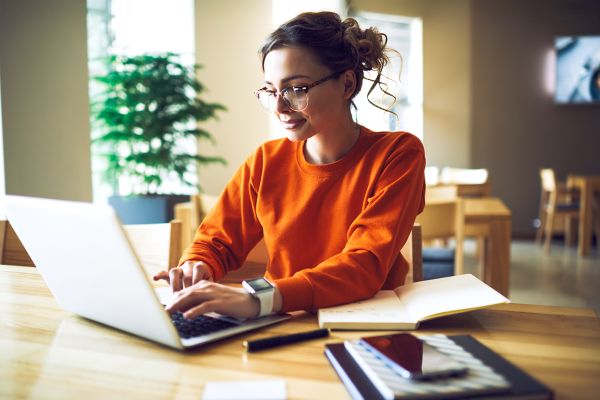 Professional young copywriter in trendy eyewear working on creation advertising content typing on laptop computer connected to wireless internet, skilled journalist browsing information in web site